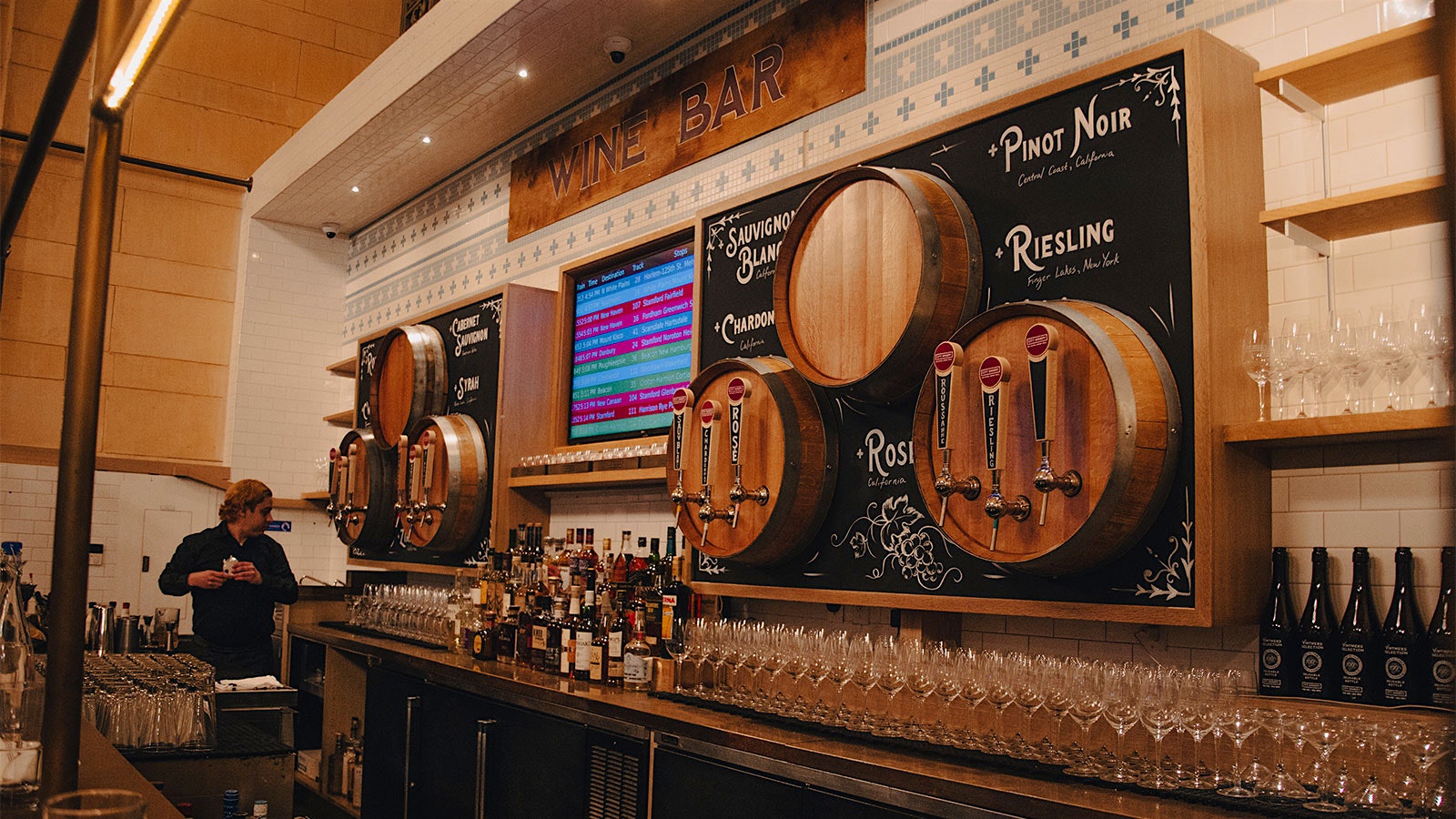  A bar at City Winery in Grand Central with wine in kegs on tap, with a screen displaying train departures.